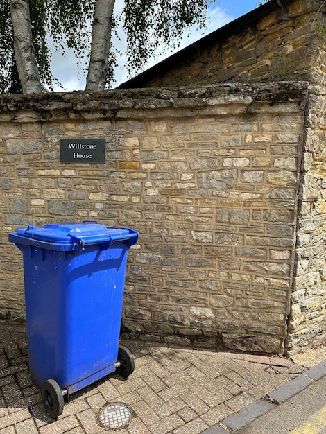 Vertical shot of a blue garbage bin in front of a brick wall