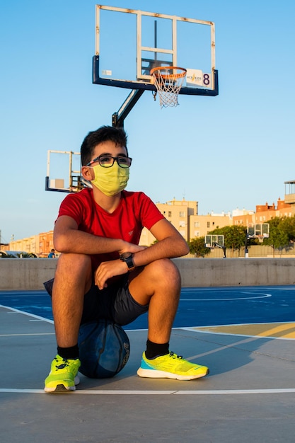 Vertical shot of a boy sitting on a ball wearing a sanitary mask-concept of the new normal