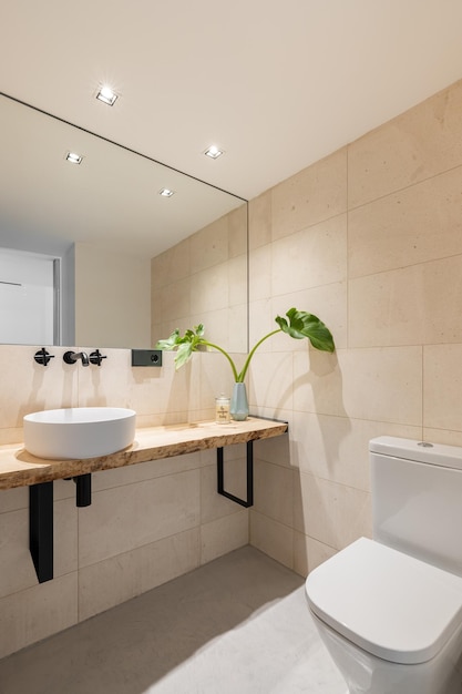 Vertical shot of a bright bathroom with beige tiles on the walls and a large mirror with a sink in a