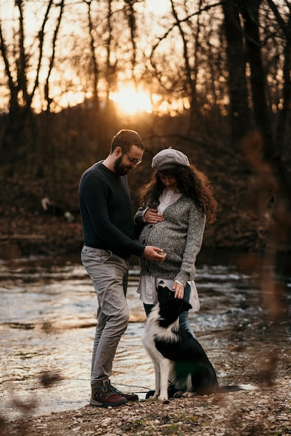 Vertical shot of a Caucasian couple with their dog doing some maternity photoshoot in the park.