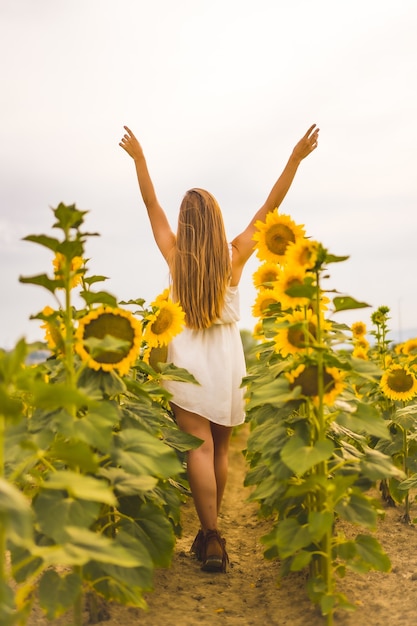 Vertical shot of a cheerful young blonde female in a sunflower field under the sunlight