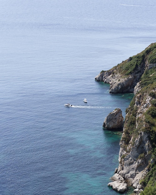 Vertical shot of cliffs covered in greenery surrounded by the sea