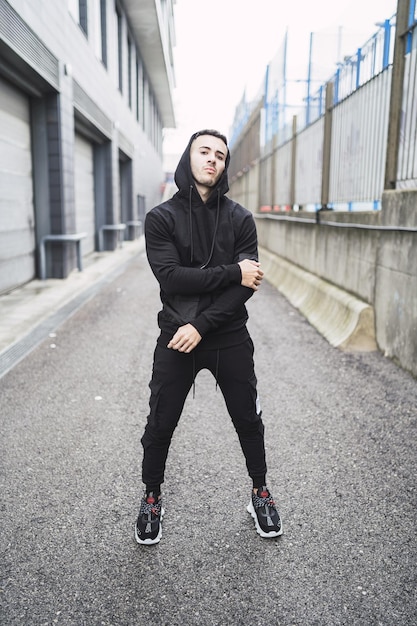 Vertical shot of a cool young man wearing a hoodie and sweatpants standing on the street