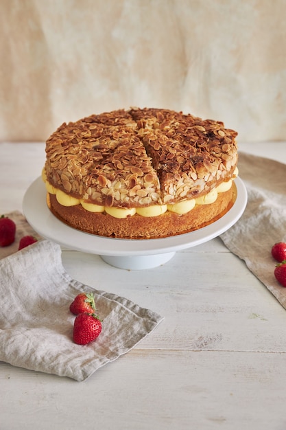 Vertical shot of a delicious cream pie with crispy almonds and strawberries on a cake stand