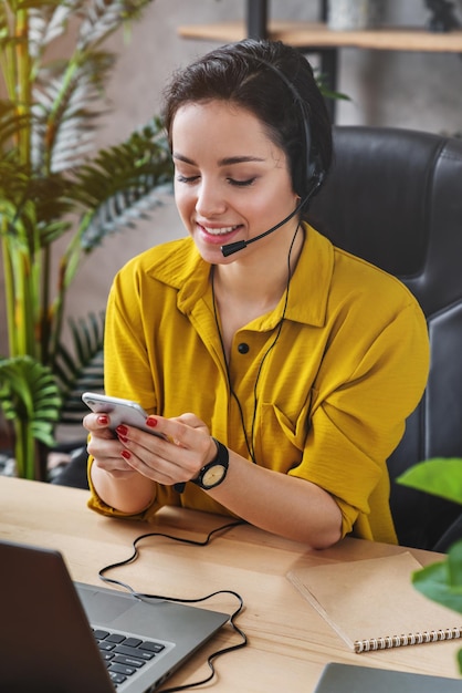 Vertical shot of female teleoperator working in home office with laptop and headset