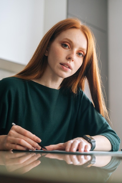 Vertical shot of focused female designer drawing making mark with pencil on white blank paper lying