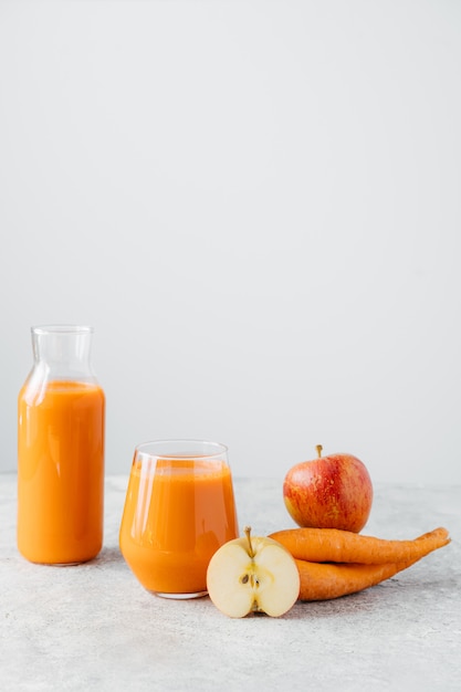 Vertical shot of fresh natural orange carrot juice in glass jar, ripe apple and carrot on white background.