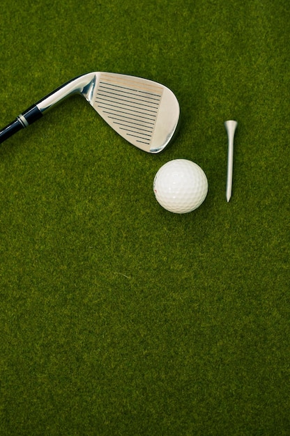 Vertical shot of a golf club, ball, and a tee on the grass with a copy space