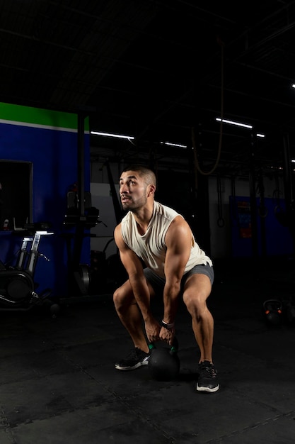 Vertical shot of a Latino man exercising in a gym using a kettlebell