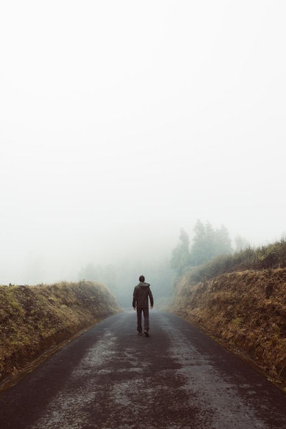 Vertical shot of a man's silhouette walking in foggy mountains