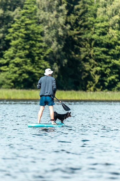 Vertical shot of a man with dog paddling with SUP on paddle board in lake. Vacation concept