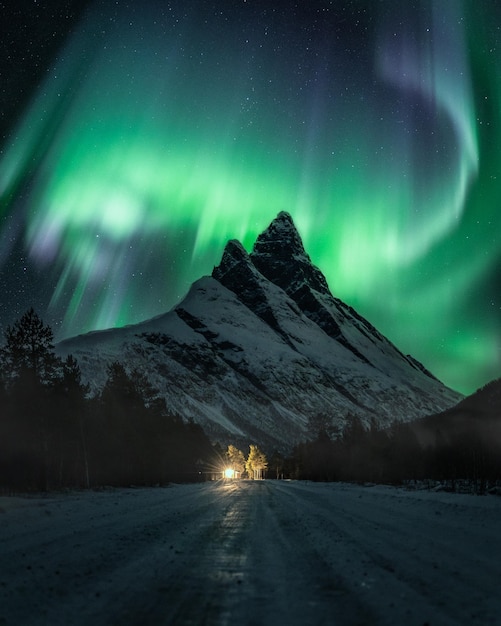 Vertical shot of a night winter landscape with a snowy road against Aurora borealis