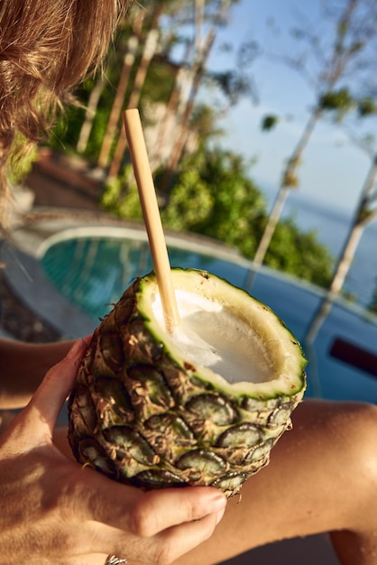 Vertical shot of a person holding a pineapple drink at the pool