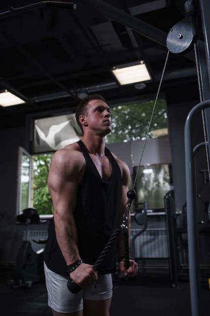 Vertical shot of a ripped male athlete doing triceps exercise in cable crossover gym machine