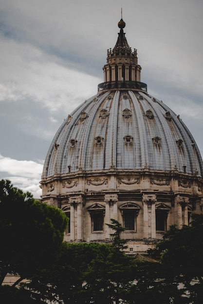 Vertical shot of the St Peter's Basilica surrounded by trees under a cloudy sky in the Vatican City