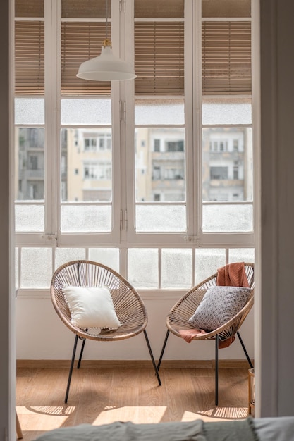 Vertical shot two cozy comfortable designer straw chairs with cushions stand on a closed loggia in a