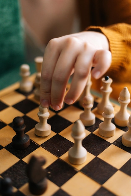 Vertical shot of unrecognizable woman making chess move with piece sitting at table in dark room selective focus