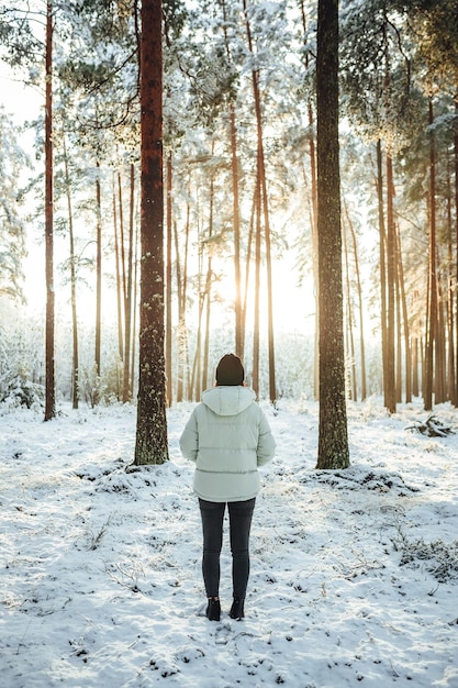 Vertical shot of the woman in a white puffer jacket against the background of snowcovered trees