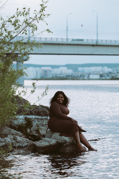 Vertical smiling barefoot bit overweight curly African American multiracial woman by the sea Summer weekend vacation