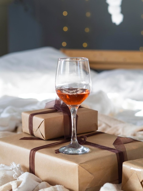 Vertical still life festive shot glass wine and gift boxes wrapped with craft brown paper on a blurred bokeh background.