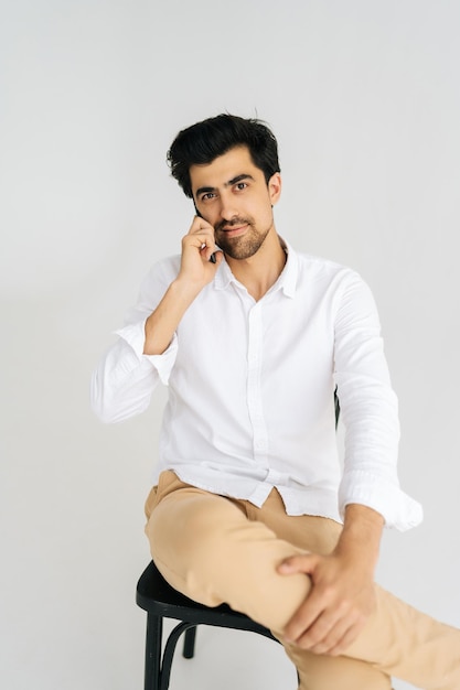 Vertical studio portrait of confident serious young business man in casual shirt talking smartphone having conversation on mobile phone looking at camera