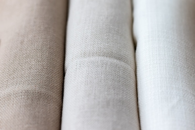 Vertical textural background of three types of natural linen fabric, rolled up. Selective focus. Closeup view