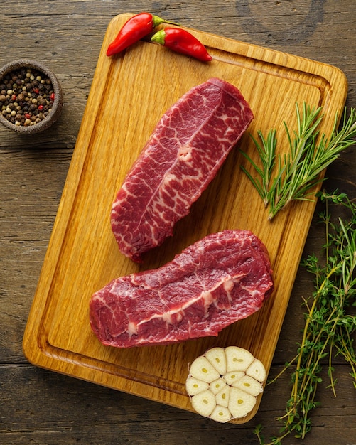 Vertical of two raw top blade beef steak on wood board with spices and herbs