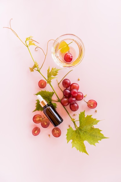 Vertical view of a cosmetic bottle and a bowl of organic apricot seed oil on a pink background with a vine high content of vitamins and minerals