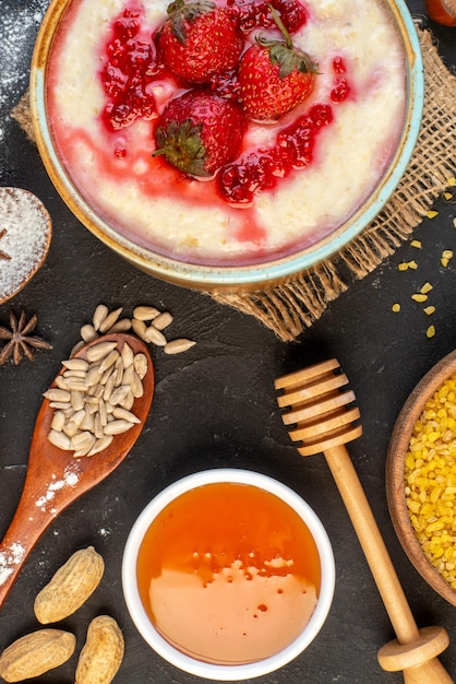 Vertical view of delicious breakfast served with strawberries jam in a bowl and spikes rice honey on dark color background