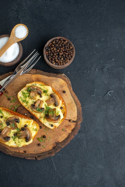 Vertical view of delicious snack with mushrooms cutlery set on wooden board and spices on black background