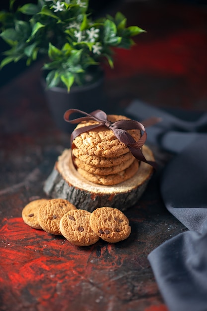 Vertical view of delicious stacked cookies tied up with ribbon on wooden board and flower pot cup of towel on dark mix colors background