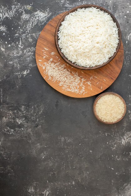 Photo vertical view of perfect long rice in a brown pot and on wooden board on the left side on gray background