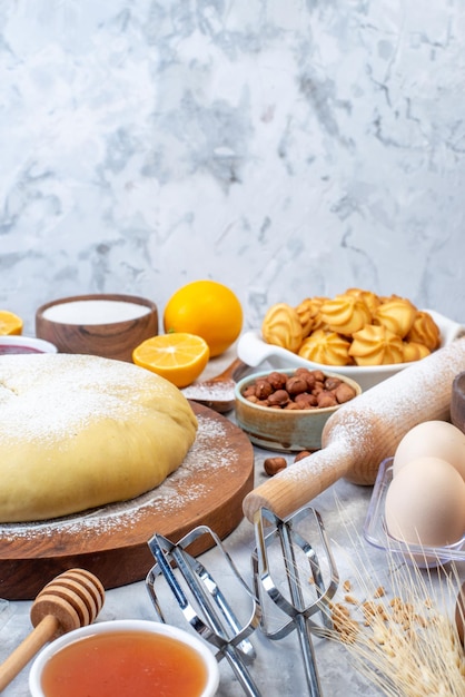 Vertical view of raw pastry on wooden round board and set of various foods grater on ice background