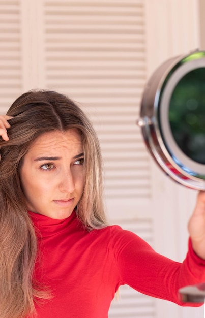 Vertical view of young blond woman looking the hair line in a round mirror about the hair loss in fall time