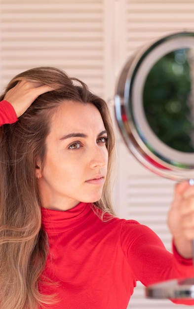 Vertical view of young woman suffering from alopecia Female hair lossWorried female looking her hairline in the mirror