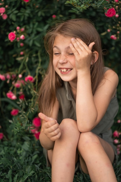 Very beautiful little girl near the roses pricked with a thorn holds her face with her hand