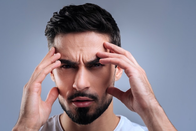 Very concentrated. Smart qualified tired worker doing his best to concentrate on the problem while touching the face with all his fingers