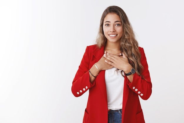 Very grateful young cute friendly-looking charming woman holding palms breast thankful smiling broadly thanking saviour help, receiving heartwarming gift, appreciate effort, white wall