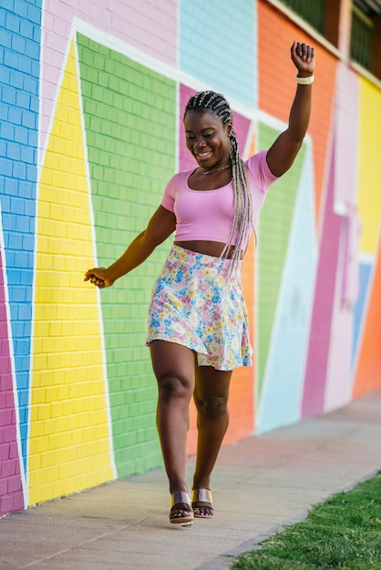 Very happy black African woman walking and posing on a wall of many colors. Lifetyle photo of a happy African woman