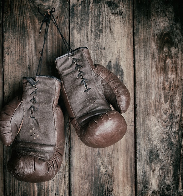 Very old leather brown boxing gloves hang on an old shabby wooden wall