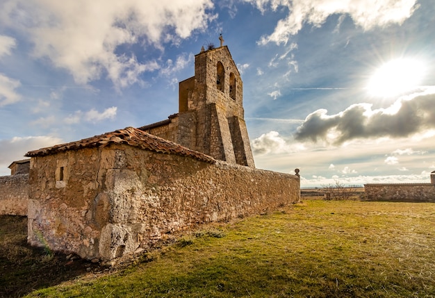 Very old stone church in the middle of the field with blue sky, clouds and sun. Rural environment. Segovia
