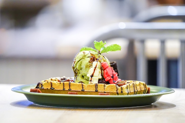 Very tasty fresh waffle with green tea icecream on top decorated by little red brown white doll white chocolate and jelly red bean beside of disk