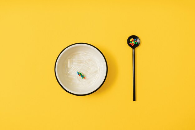 Vibrant colorful flat lay of medicine pill capsules filled with sugar candy sprinkles on yellow background. Creative concept of overdose medicine usage and addiction to food supplement.