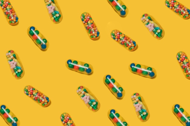 Vibrant colorful pattern of medicine pill capsules filled with sugar candy sprinkles on yellow background Creative concept of overdose medicine usage and addiction to food supplement Placebo