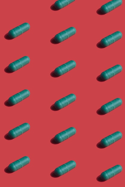 Vibrant colourful pattern of green medicine pill capsules on red background. 