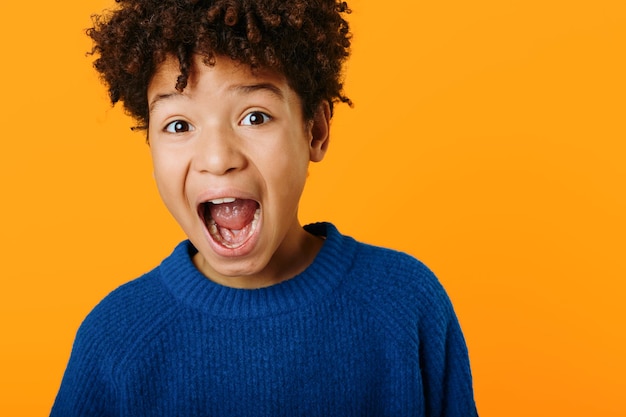 Vibrant portrait of excited young african american boy expressing joy with wide open mouth against a bright orange background