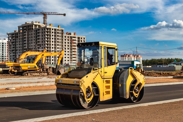 Vibratory road roller lays asphalt on a new road under construction. Close-up of the work of road machinery. Construction work on the construction of urban highways.