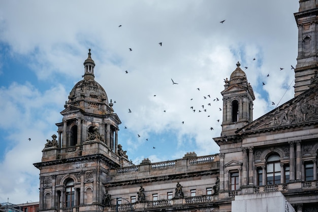 The victorian and beaux arts style city chambers of glasgow with birds flying in the sky over it