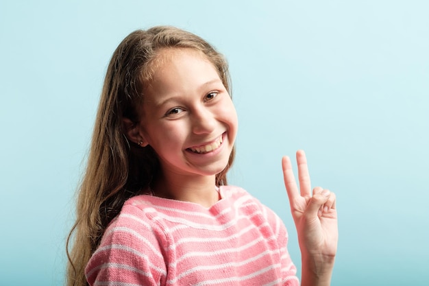 Victory sign piece gesture smiling adolescent girl portrait on blue background