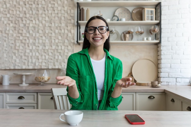 Video blogger a young beautiful woman in glasses and a green shirt sits in front of a web camera at